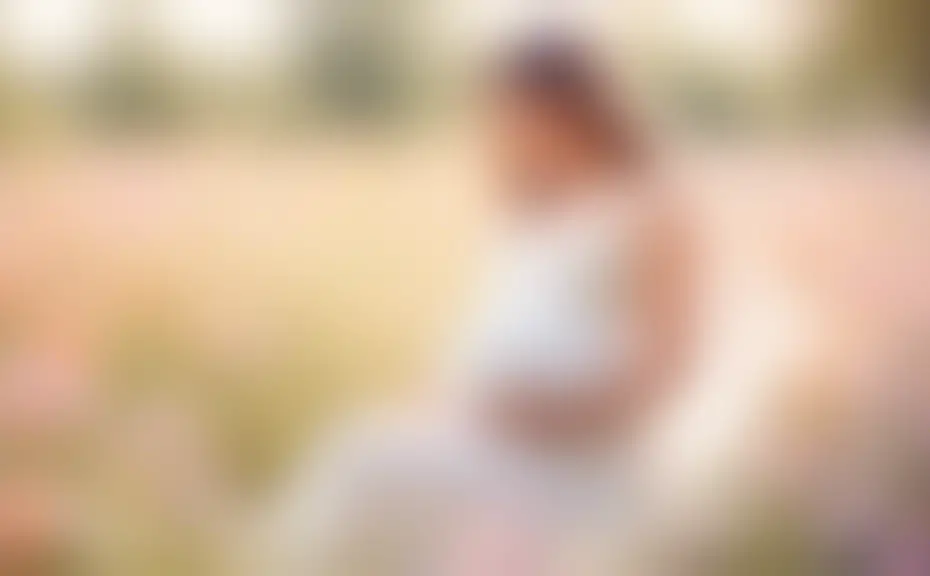 Serene maternity photoshoot in a sunlit wildflower meadow, featuring a happy expectant mother in a flowing white dress, softly cradling her belly, surrounded by nature, with gentle expressions and pas